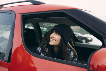 Lächelnde Frau, die wegschaut, während sie in einem roten Auto sitzt - MASF08164