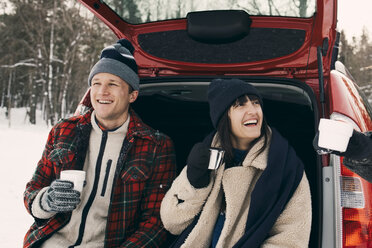 Happy woman having coffee while sitting with friends in car trunk during winter - MASF08165