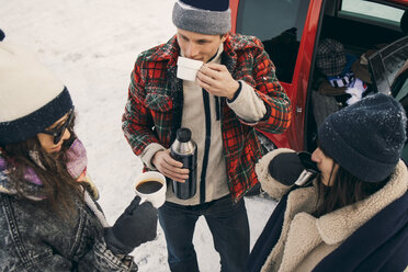 Hohe Winkelansicht von Freunden, die Kaffee trinken, während sie sich im Auto auf Schnee unterhalten - MASF08169