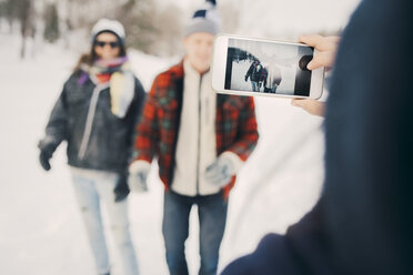 Frau fotografiert Freunde mit dem Smartphone auf einem Feld im Winter - MASF08182