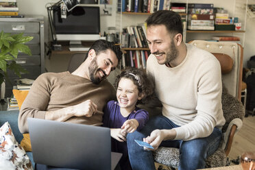 Glückliche Väter mit Tochter beim Online-Shopping am Laptop mit Kreditkarte, während sie zu Hause auf Stühlen sitzen - MASF08194