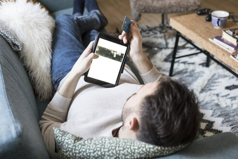 Hoher Blickwinkel eines jungen Mannes beim Online-Shopping auf einem digitalen Tablet mit Kreditkarte, während er sich zu Hause auf dem Sofa entspannt - MASF08195