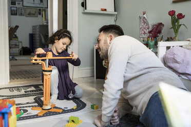 Vater betrachtet Tochter beim Spielen mit Kranspielzeug im Wohnzimmer zu Hause - MASF08197