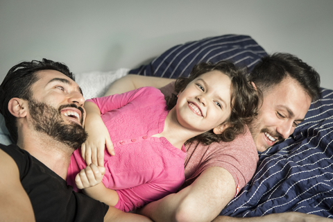 Fröhliche Tochter spielt mit Vätern auf dem Bett im Schlafzimmer zu Hause, lizenzfreies Stockfoto