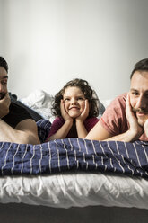 Fathers and daughter lying with head in hands on bed against wall - MASF08204