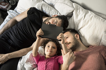 Daughter and fathers looking at digital tablet while lying on bed in bedroom - MASF08208