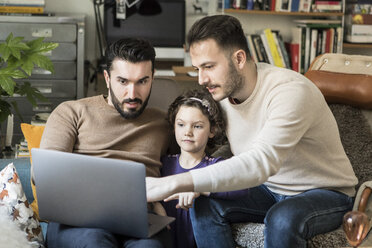 Väter zeigen ihrer Tochter den Laptop, während sie zu Hause auf einem Stuhl sitzen - MASF08210