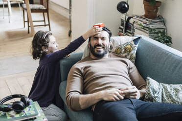 High angle view of girl keeping toy block on father's head lying on sofa at home - MASF08220