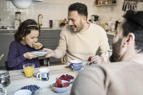 Lachender Vater hält Teller, während Tochter am Tisch Pfannkuchen isst - MASF08225