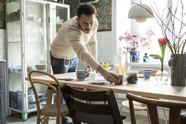 Young man arranging cup on table in kitchen at home - MASF08229