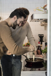 Lächelnder schwuler Mann, der mit seinem Partner in der Küche steht und Teig in einen Kochtopf gießt - MASF08230