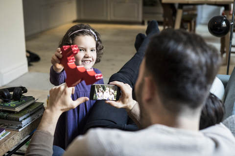 Lächelnde Tochter zeigt rotem Block zu Vätern im Wohnzimmer ausruhen, lizenzfreies Stockfoto