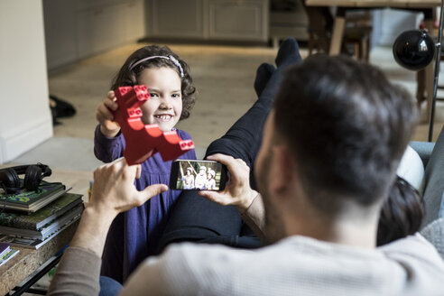 Lächelnde Tochter zeigt rotem Block zu Vätern im Wohnzimmer ausruhen - MASF08235