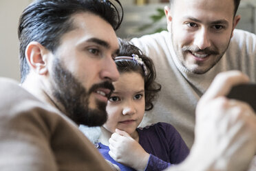 Väter mit neugieriger Tochter, die auf ihr Smartphone schaut, während sie zu Hause sitzen - MASF08237