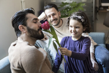 Lächelnde Tochter lässt Vater an Tulpen riechen, während sie mit einem Mann auf dem Sofa im Wohnzimmer sitzt - MASF08239