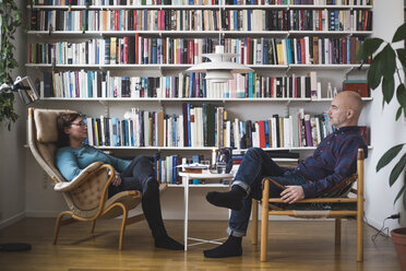 Full length of therapist and patient discussing by bookshelf at home office - MASF08251