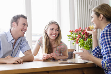 Drei junge Leute, die an einem Tisch sitzen, sich unterhalten und lächeln - CUF40103