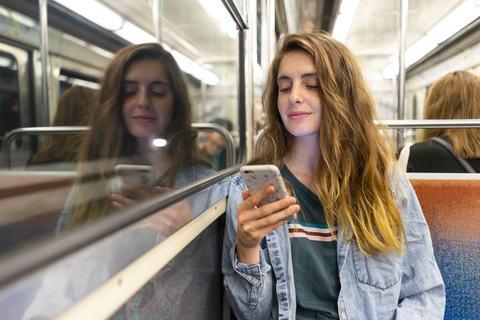 Smiling young woman in underground train looking at smartphone stock photo