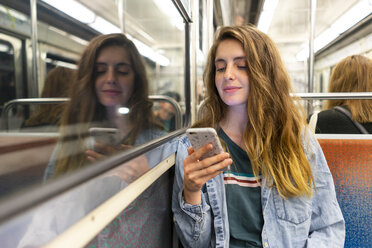 Lächelnde junge Frau in der U-Bahn, die auf ihr Smartphone schaut - AFVF00743