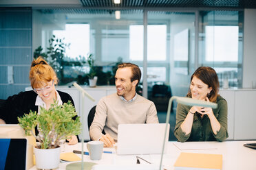 Cheerful business colleagues discussing while sitting at desk in creative office - MASF08258