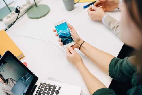 Hohe Winkel Ansicht der Geschäftsfrau mit Smartphone während des Sitzens mit Laptop am Schreibtisch im kreativen Büro - MASF08267