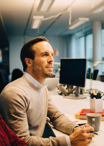 Selbstbewusster Geschäftsmann, der an einem beleuchteten Schreibtisch in einem kreativen Büro sitzt, lizenzfreies Stockfoto