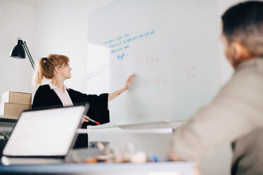 Low angle view of young businesswoman standing by acrylic glass with colleague in board room at office - MASF08278