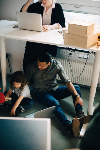 Hohe Winkel Ansicht von Vater und Sohn sitzen mit Laptop von Geschäftsfrau arbeiten im kreativen Büro, lizenzfreies Stockfoto