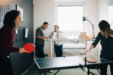 Weibliche Fachkräfte spielen Tischtennis, während männliche Kollegen im Kreativbüro einen Laptop benutzen - MASF08285