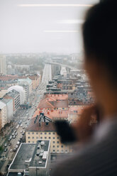 Ausgeschnittenes Bild eines Geschäftsmannes, der durch ein Fenster im Kreativbüro auf die Stadtlandschaft blickt - MASF08294