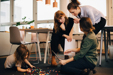 Female colleagues discussing over laptop by boy playing on floor at creative office - MASF08296