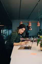 Side view of businesswoman using smart phone while working at desk in creative office - MASF08302