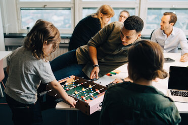 Hoher Blickwinkel auf einen Jungen, der mit einem Geschäftsmann auf dem Schreibtisch inmitten von Kollegen im Kreativbüro Tischfußball spielt - MASF08305