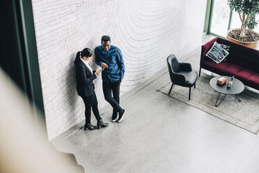 Geschäftspartner in voller Länge im Gespräch, während sie sich bei einer Bürokonferenz an die Wand lehnen - MASF08373