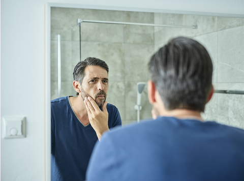 Serious man looking in bathroom mirror stock photo