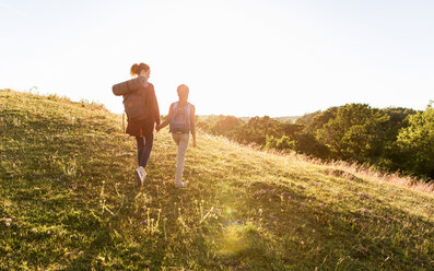 Rückansicht in voller Länge von Mutter und Tochter, die sich an den Händen halten, während sie auf einem Hügel im Park bei Sonnenuntergang wandern - MASF08436