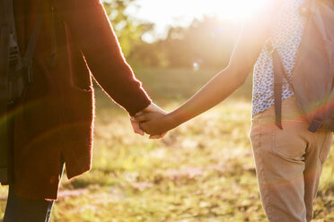 Midsection of mother and daughter holding hands at park during sunset - MASF08438