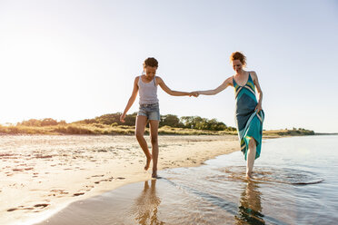 Full length of mother and daughter holding hands while walking on shore at beach against clear sky - MASF08442