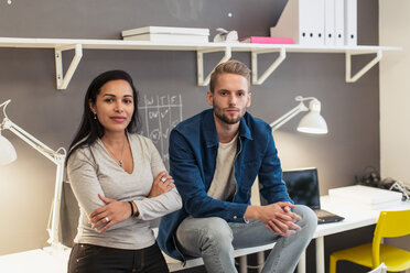 Portrait of confident business colleagues sitting on desk against wall at creative office - MASF08455