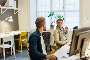 Colleagues discussing while sitting at desk in illuminated creative office - MASF08469