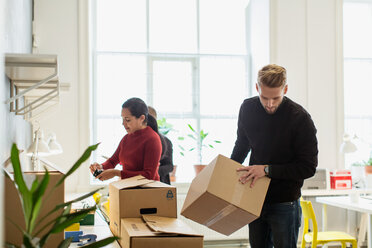 Junger Geschäftsmann ordnet Karton von weiblichen Kollegen, die in einem kreativen Büro arbeiten - MASF08476