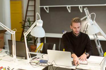 Selbstbewusster junger Mann arbeitet an einem beleuchteten Schreibtisch in einem kreativen Büro - MASF08489