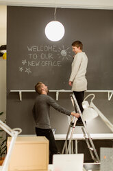 Happy colleagues standing by wall in illuminated creative office - MASF08502