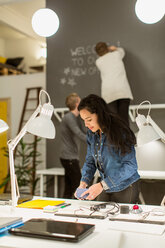 Mid adult businesswoman arranging desk against colleagues working in creative office - MASF08504