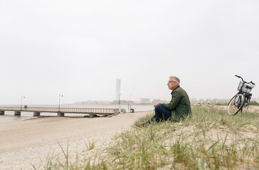 Voller Länge von älteren männlichen Pendler sitzen auf Sand am Strand gegen klaren Himmel - MASF08511