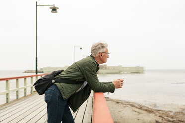 Seitenansicht eines älteren Mannes, der sich auf die Reling stützt und das Meer gegen den klaren Himmel betrachtet - MASF08513