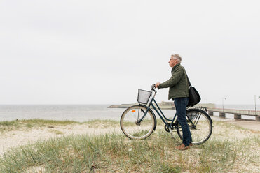 Full length side view of senior male commuter standing with bicycle at beach against clear sky - MASF08515