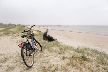 Seitenansicht eines älteren männlichen Pendlers, der mit seinem Fahrrad am Strand sitzt, bei klarem Himmel - MASF08517