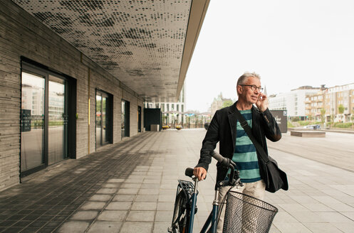 Älterer Mann spricht mit seinem Smartphone, während er mit dem Fahrrad in der Stadt steht - MASF08518