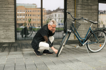 Voller Länge der älteren Mann spricht durch Smartphone bei der Überprüfung Fahrradreifen gegen Gebäude in der Stadt - MASF08519